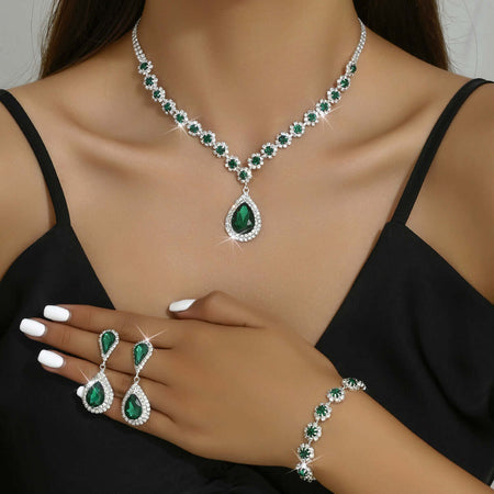 Elegant woman wearing green gemstone necklace, matching earrings, ring, and bracelet set with sparkling details.